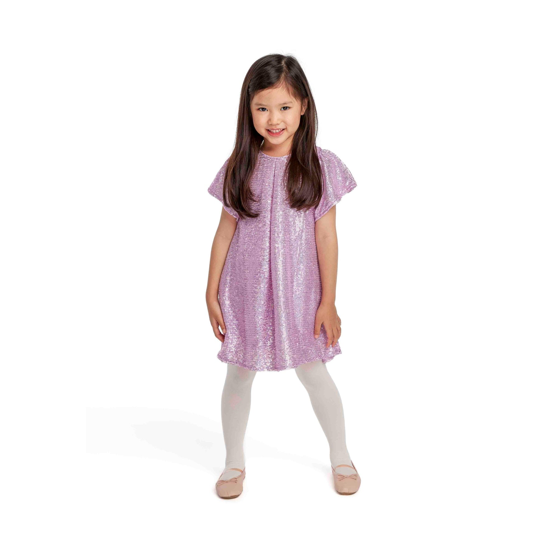 Young girl wearing sparkly pink sequin dress with short sleeves and white tights, standing against white background with hands by her sides