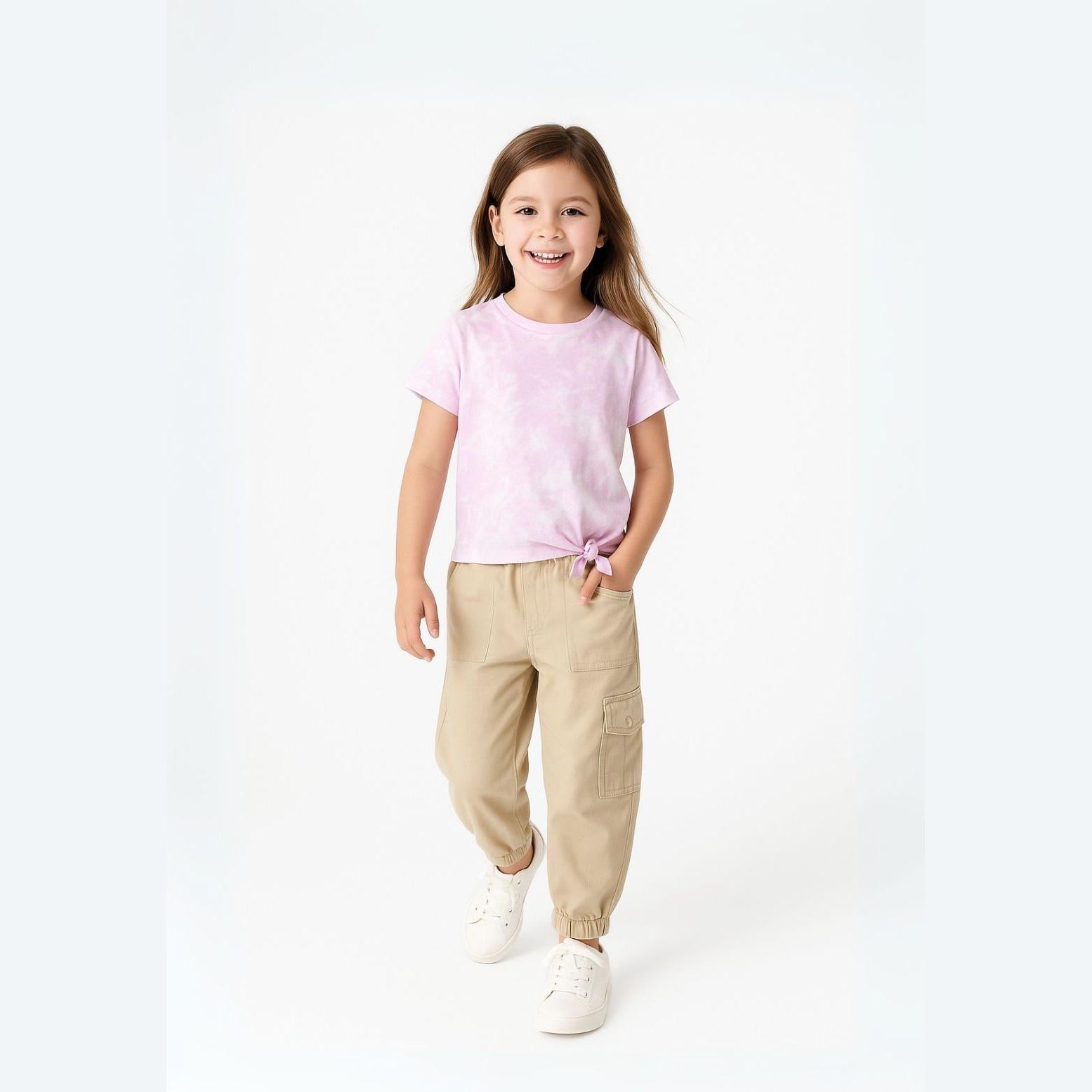 Young girl wearing beige combat trousers with paperbag waist and pink tie-front t-shirt, standing against white background