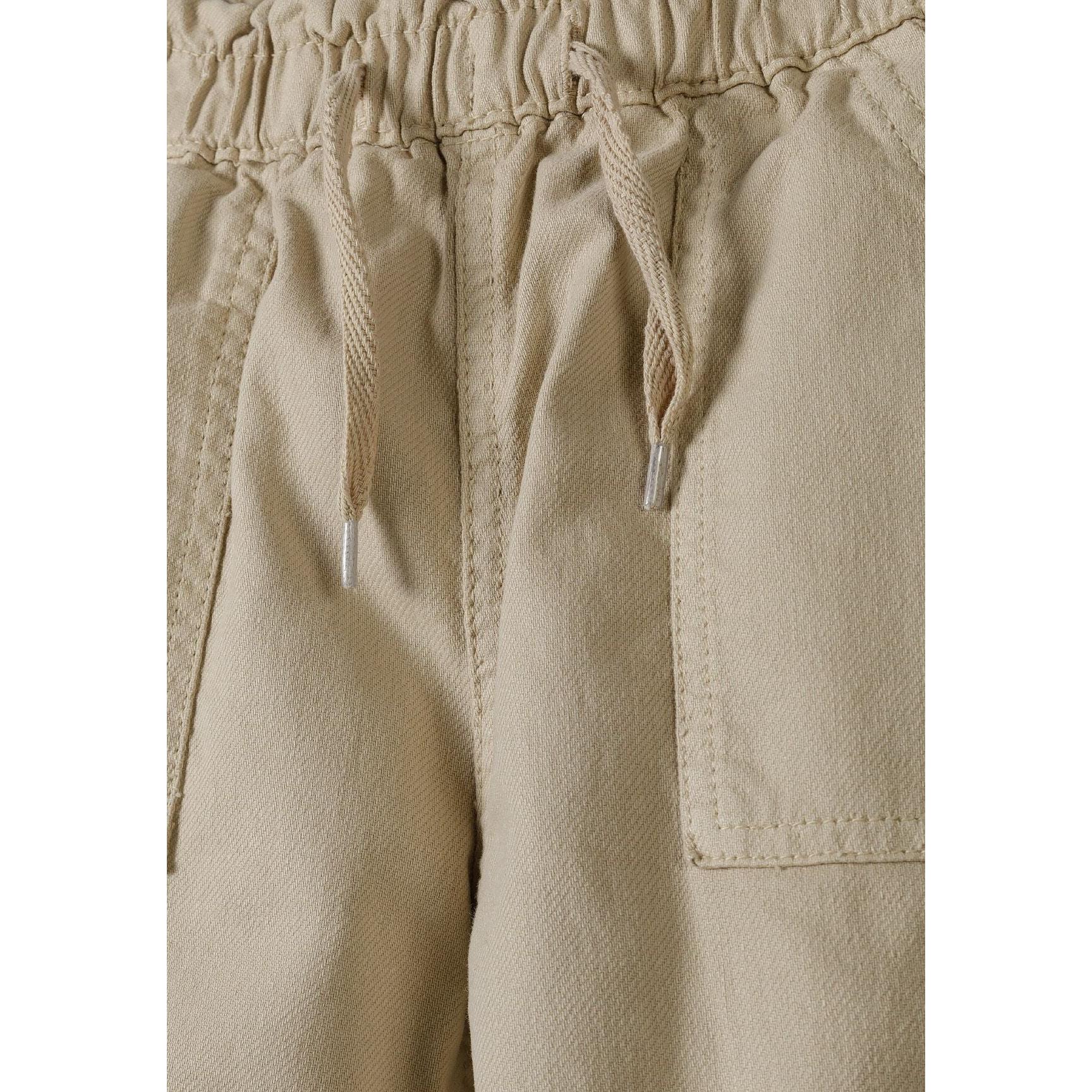 Close-up detail of beige combat trousers waistband showing drawstring ties and gathered paperbag styling